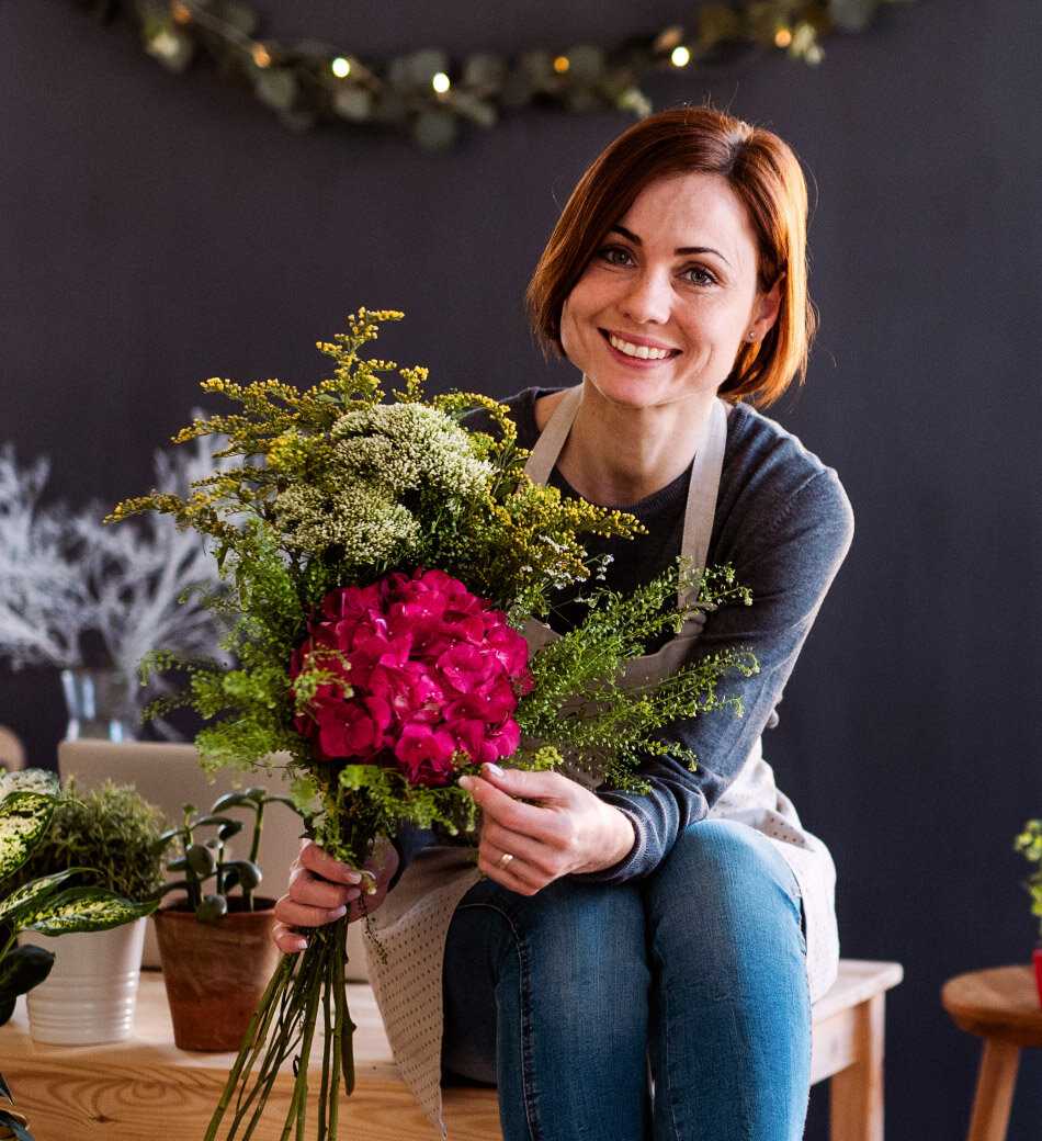 A female florist sitting on a table holding a bunch of beautiful red flowers